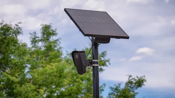 A Flock Safety automated license-plate-reader camera mounted below a solar panel on a roadside pole.