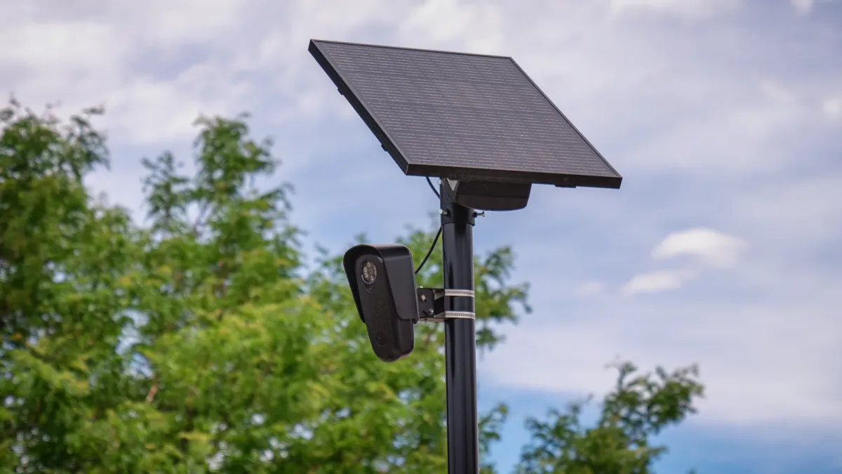 A Flock Safety automated license-plate-reader camera mounted below a solar panel on a roadside pole.